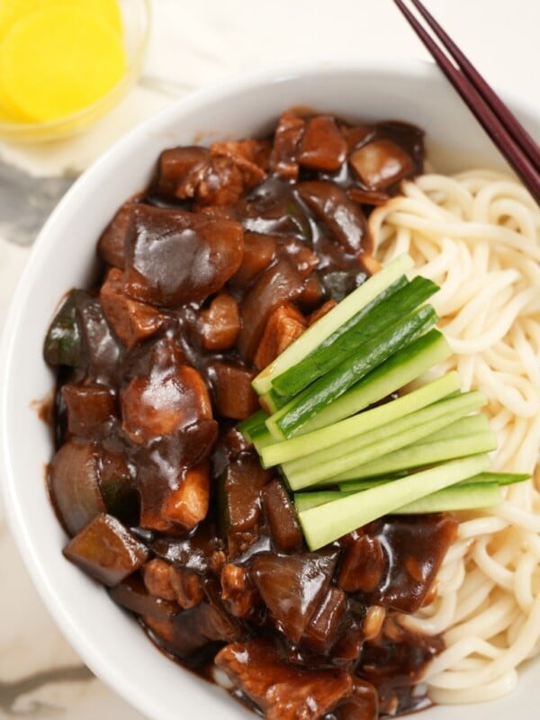 Jajangmyeon plated in a bowl with sliced cucumbers and radish.