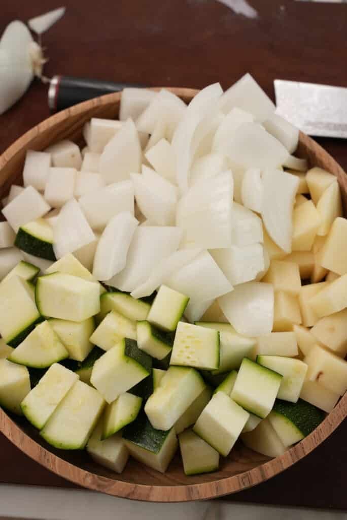Cubed potatoes, zucchini, radish, and onions in a wooden bowl.