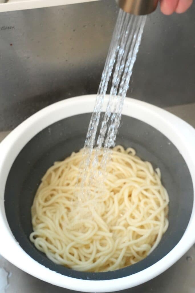 Rinsing Korean wheat noodles with cold water in a colander.