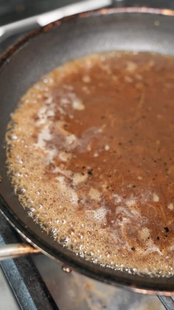 Beef broth reducing in a pan.