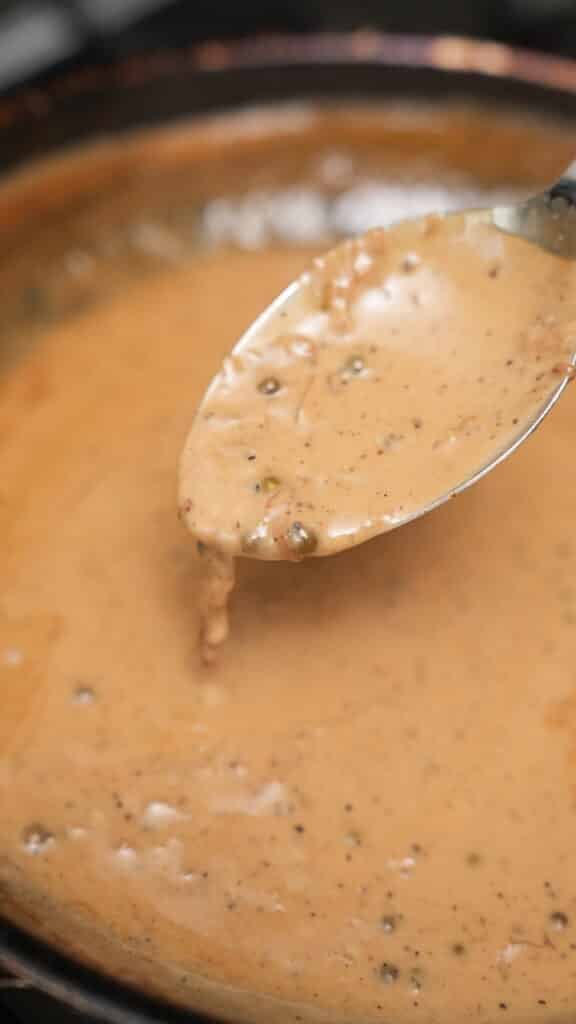 Peppercorn sauce in a spoon over a pan.