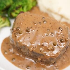 A piece of steak covered with peppercorn sauce next to mashed potatoes and broccoli.