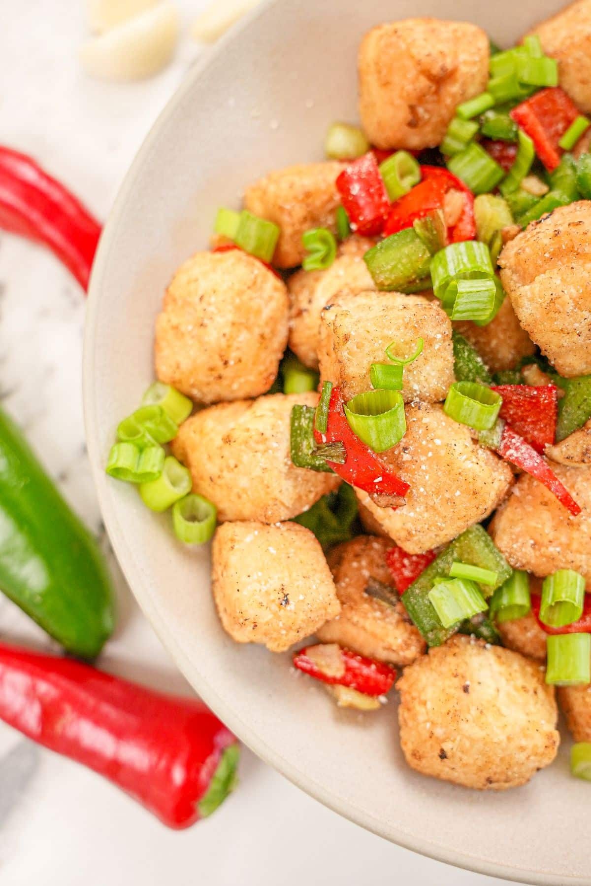 Salt and pepper tofu in a bowl with peppers and seasonings.