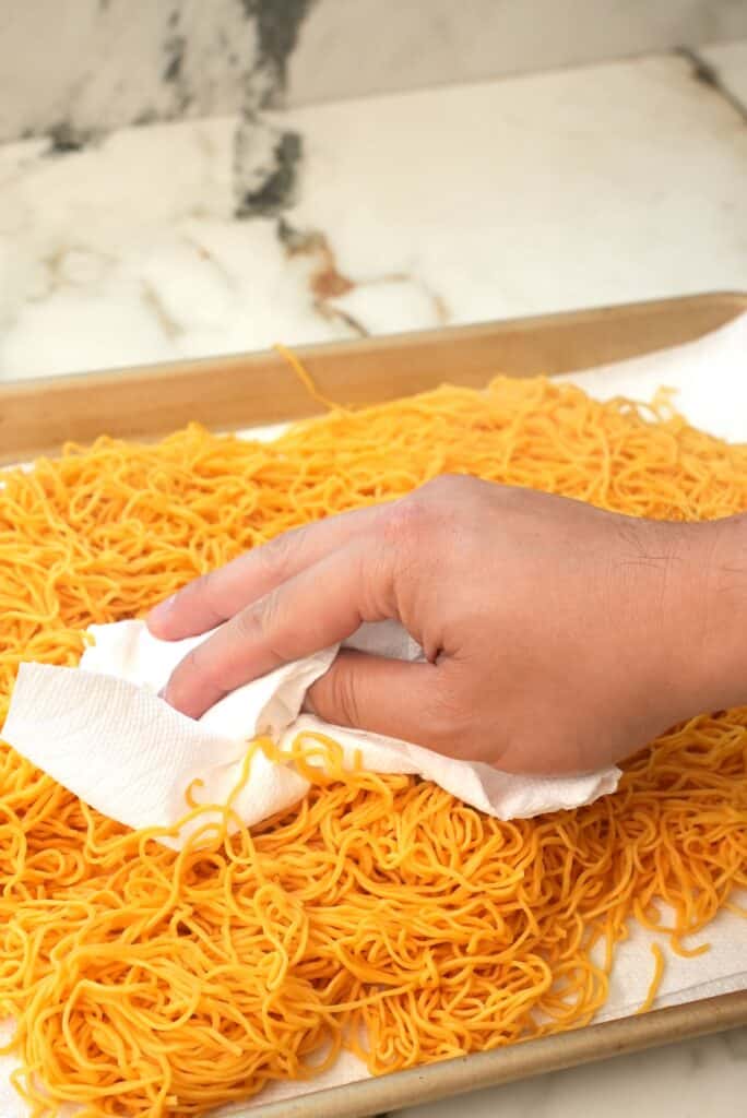 A hand patting the noodles dry with a paper towel.