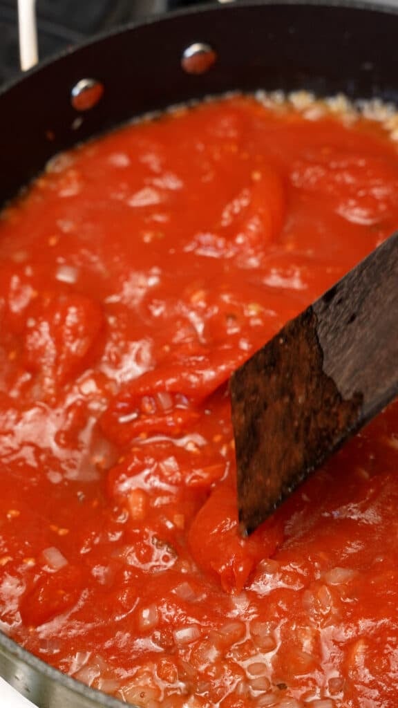 A wooden spatula mixing tomato sauce in a pan.
