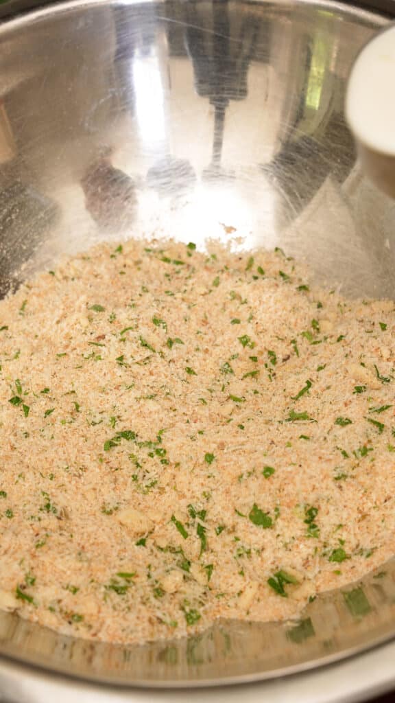 Breadcrumbs seasoned with garlic, salt, pepper, parsley, oregano and parmesan cheese in a metal mixing bowl.