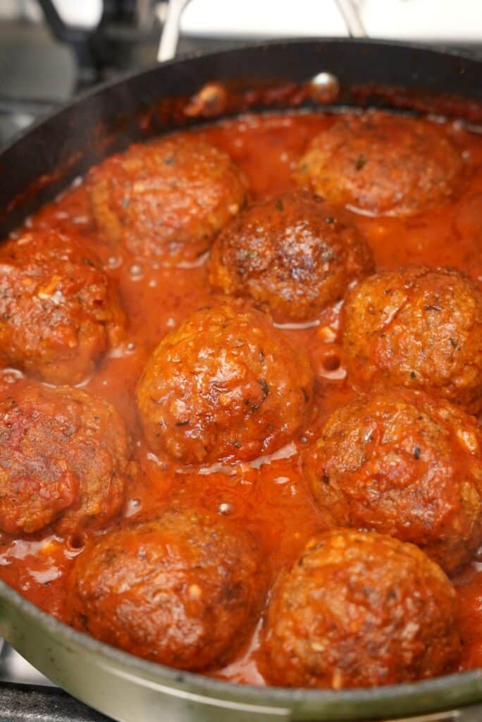 Meatballs simmering in tomato sauce in a pan.