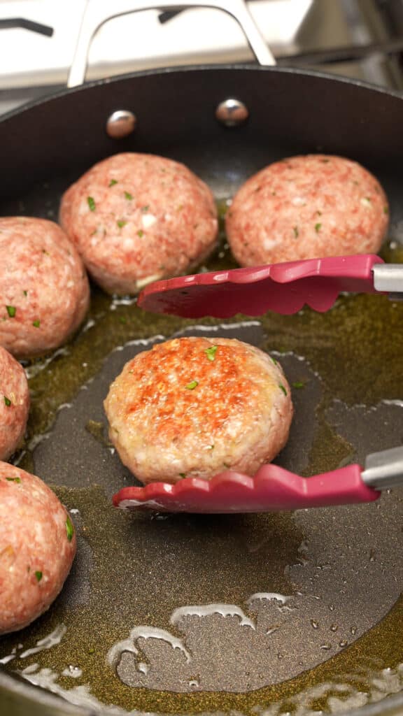Meatballs frying in olive oil in a pan.