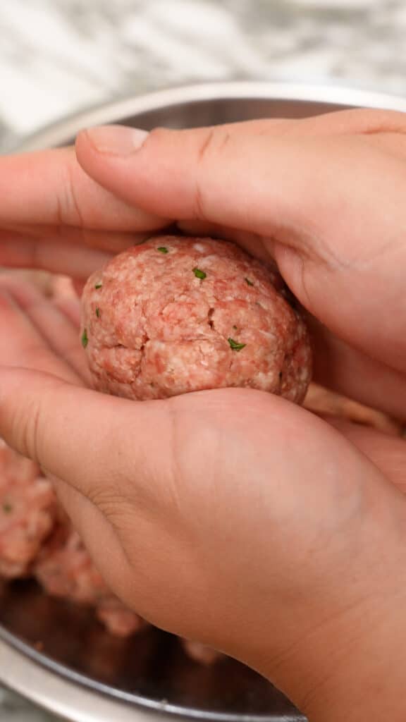 Hands rolling the meat mixture into meatballs.
