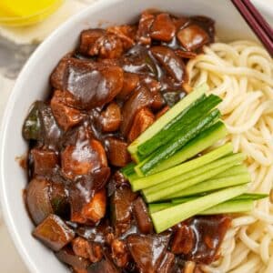 Jajangmyeon in a bowl with cucumbers and yellow pickled radish.