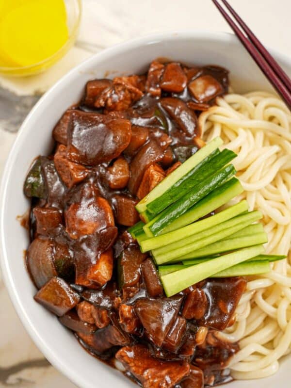 Jajangmyeon in a bowl with cucumbers and yellow pickled radish.