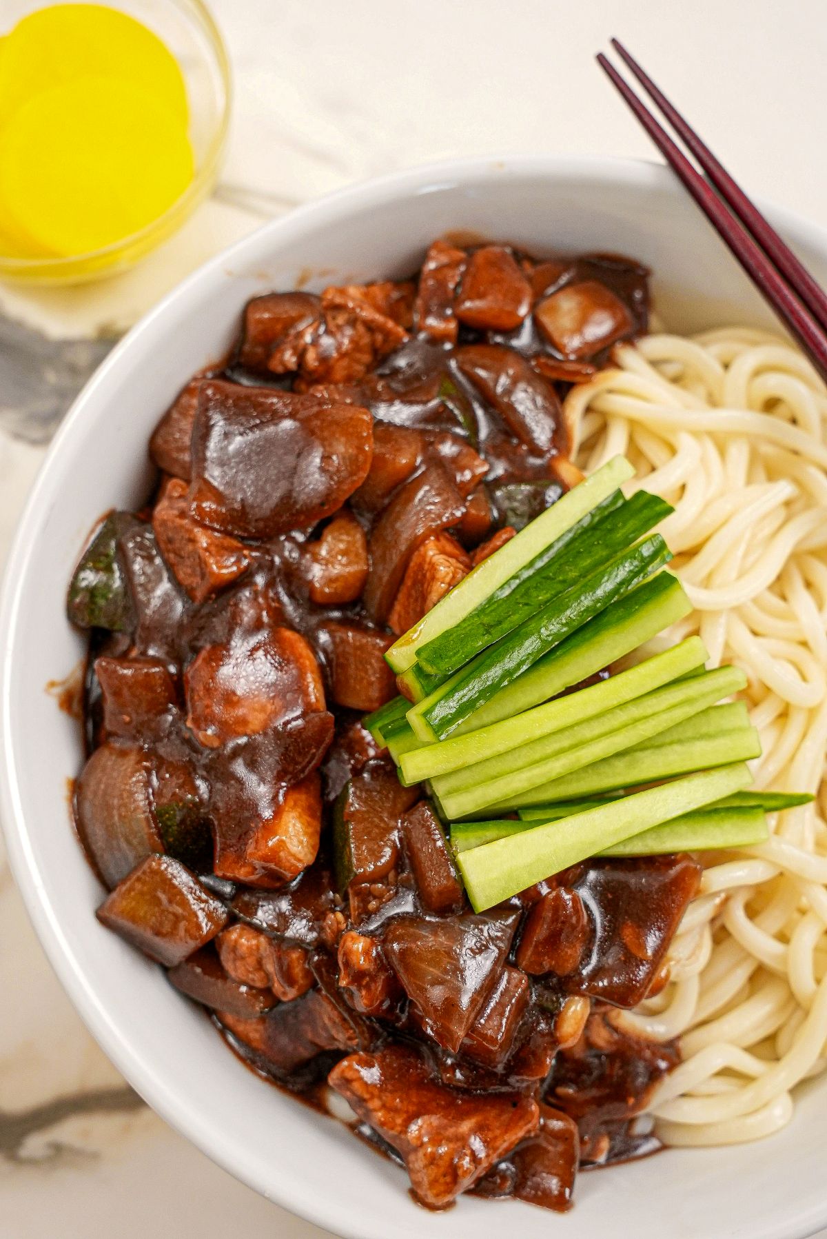 Jajangmyeon in a bowl with cucumbers and yellow pickled radish.