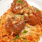 Spaghetti and Meatballs on a white plate topped with parmesan cheese and parsley.