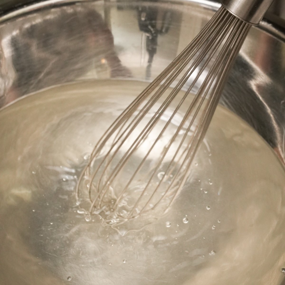 A whisk mixing together a brining solution of water, salt, and sugar for brining chicken tenders.