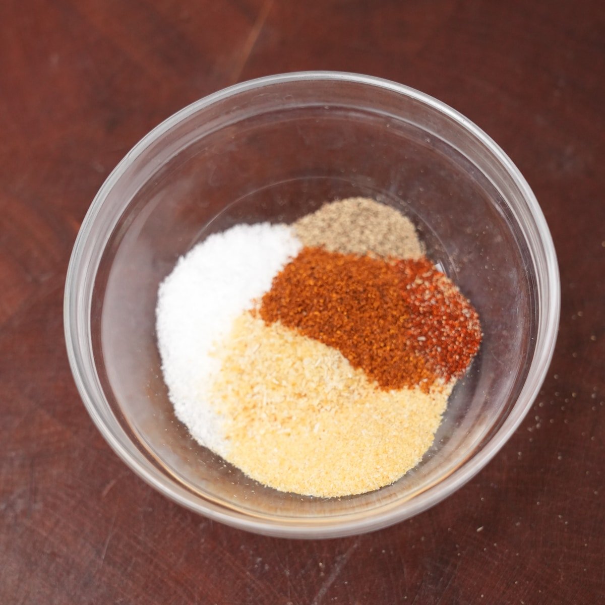 A seasoning mix of salt, pepper, garlic powder, onion powder, paprika, and cayenne pepper in a small glass bowl.
