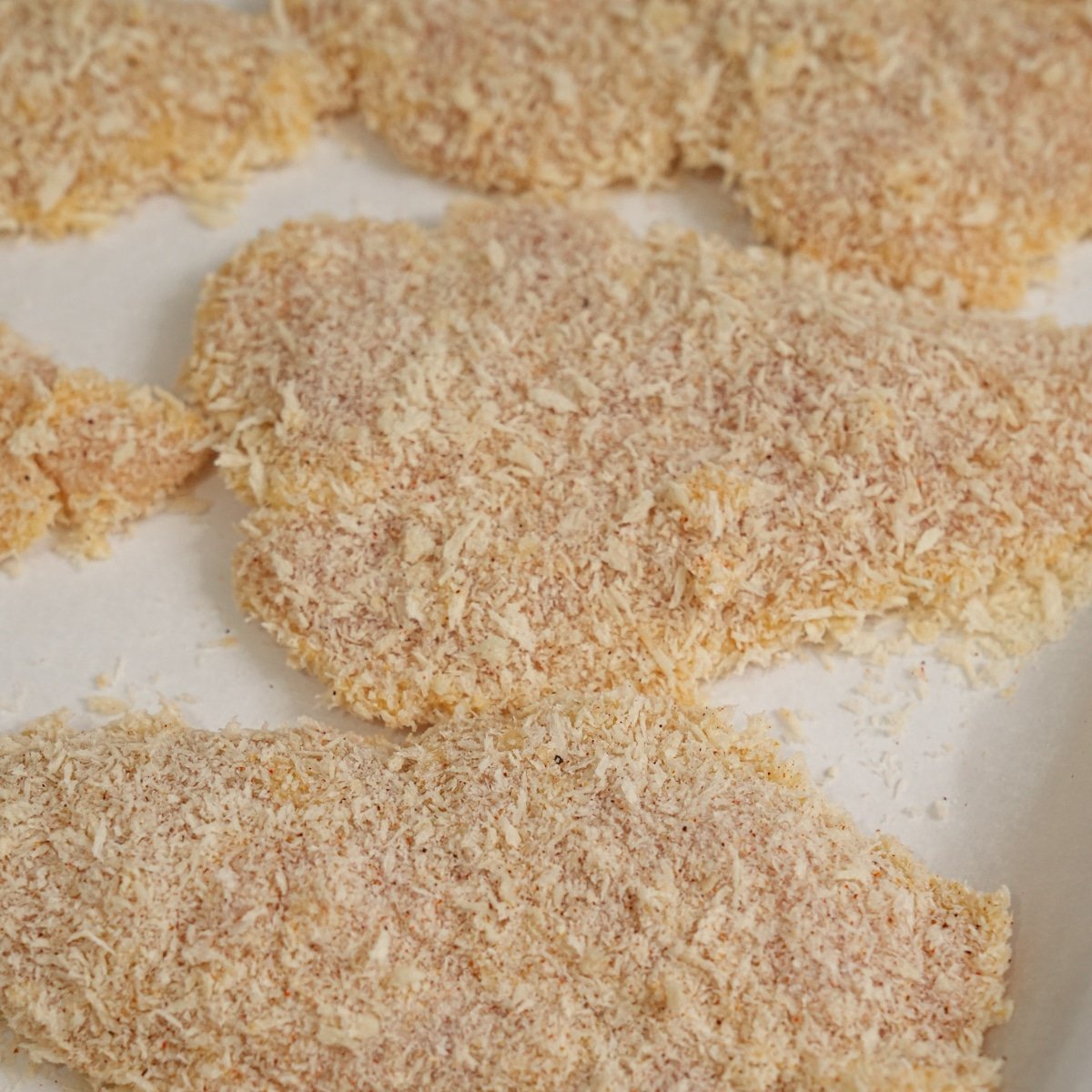 Breaded chicken tenders laying on a parchment paper lined baking sheet.