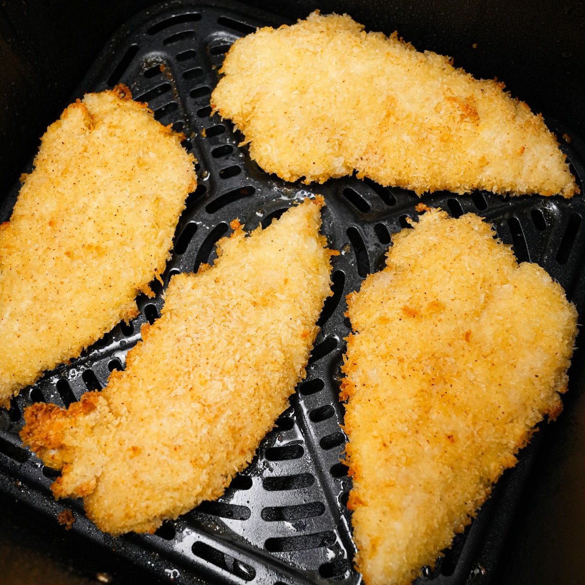 Breaded chicken tenders laying in a single layer in an air fryer basket.