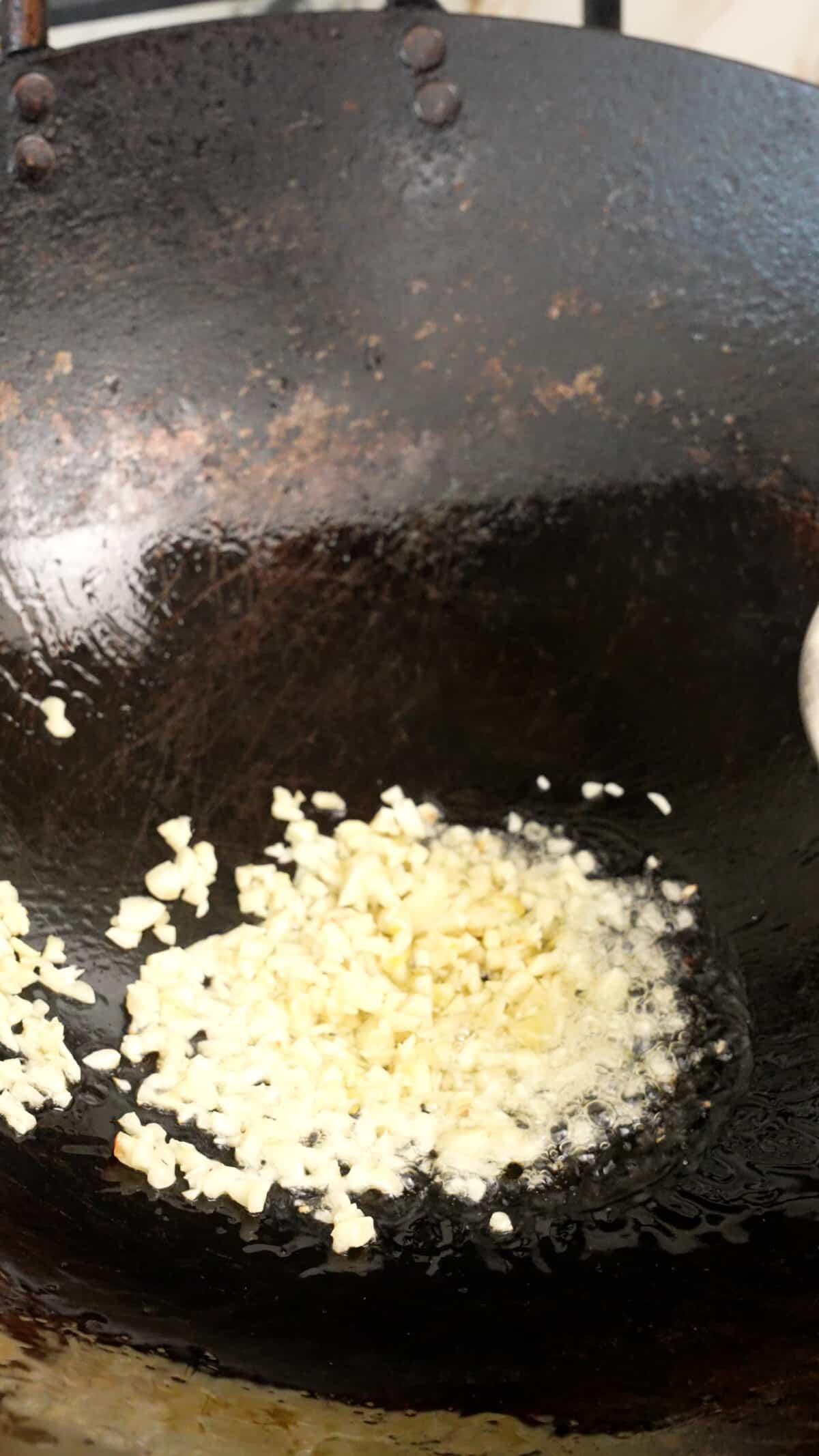 Garlic sauteing in a wok with oil.