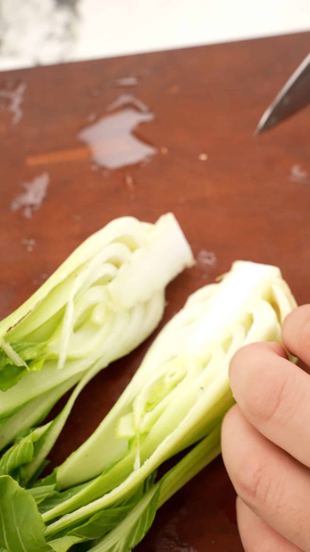 Baby bok choy sliced in half with a knife on a cutting board.