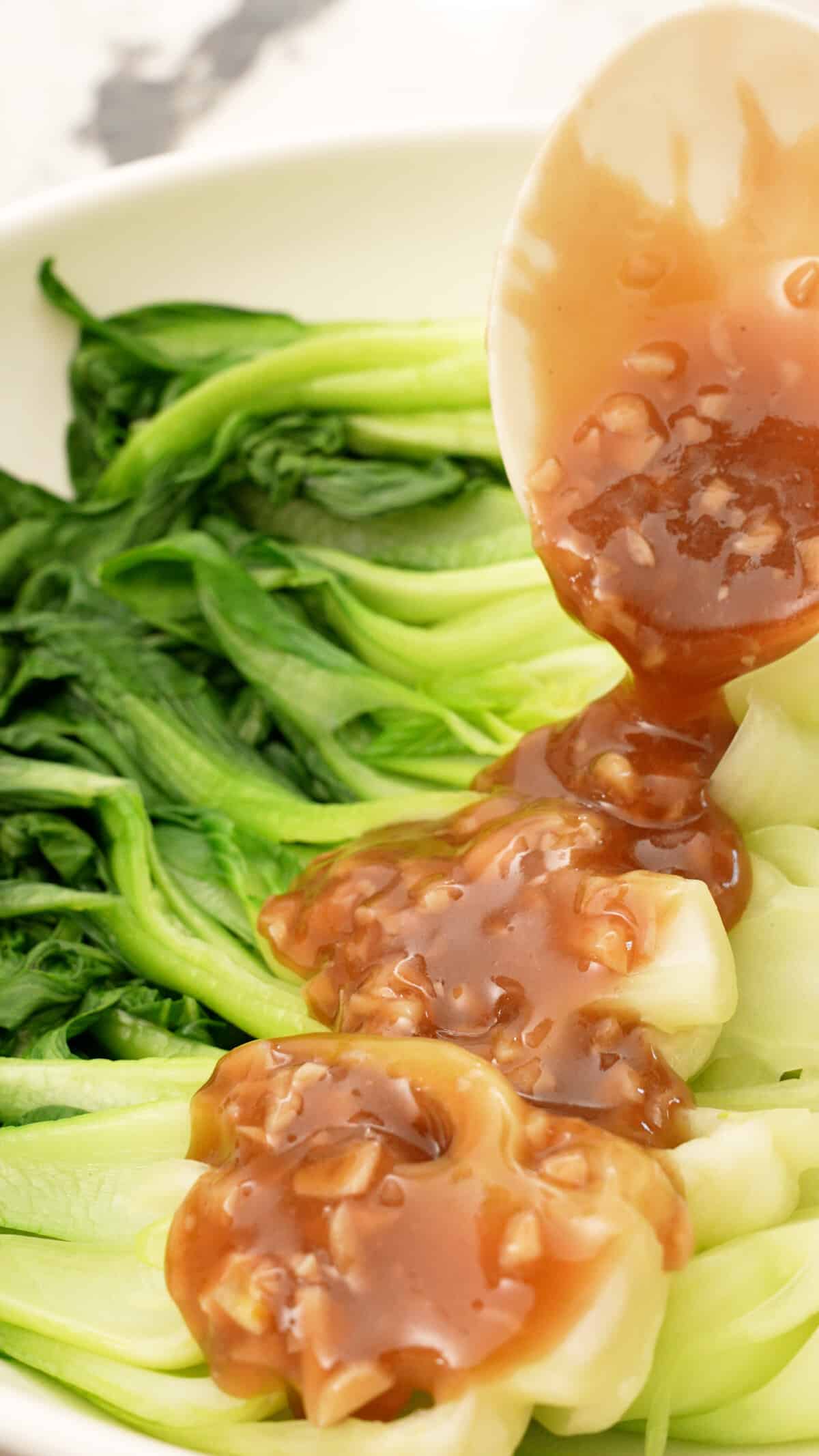 Bok choy with garlic sauce being ladled on top.