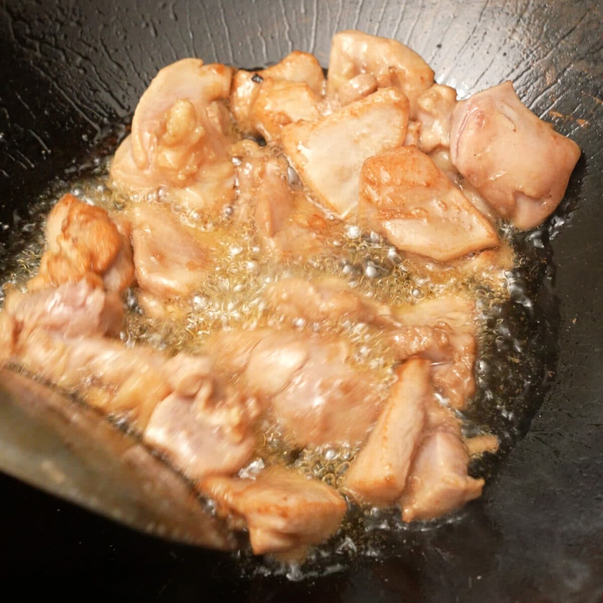 Chicken cooking in oil in a wok.