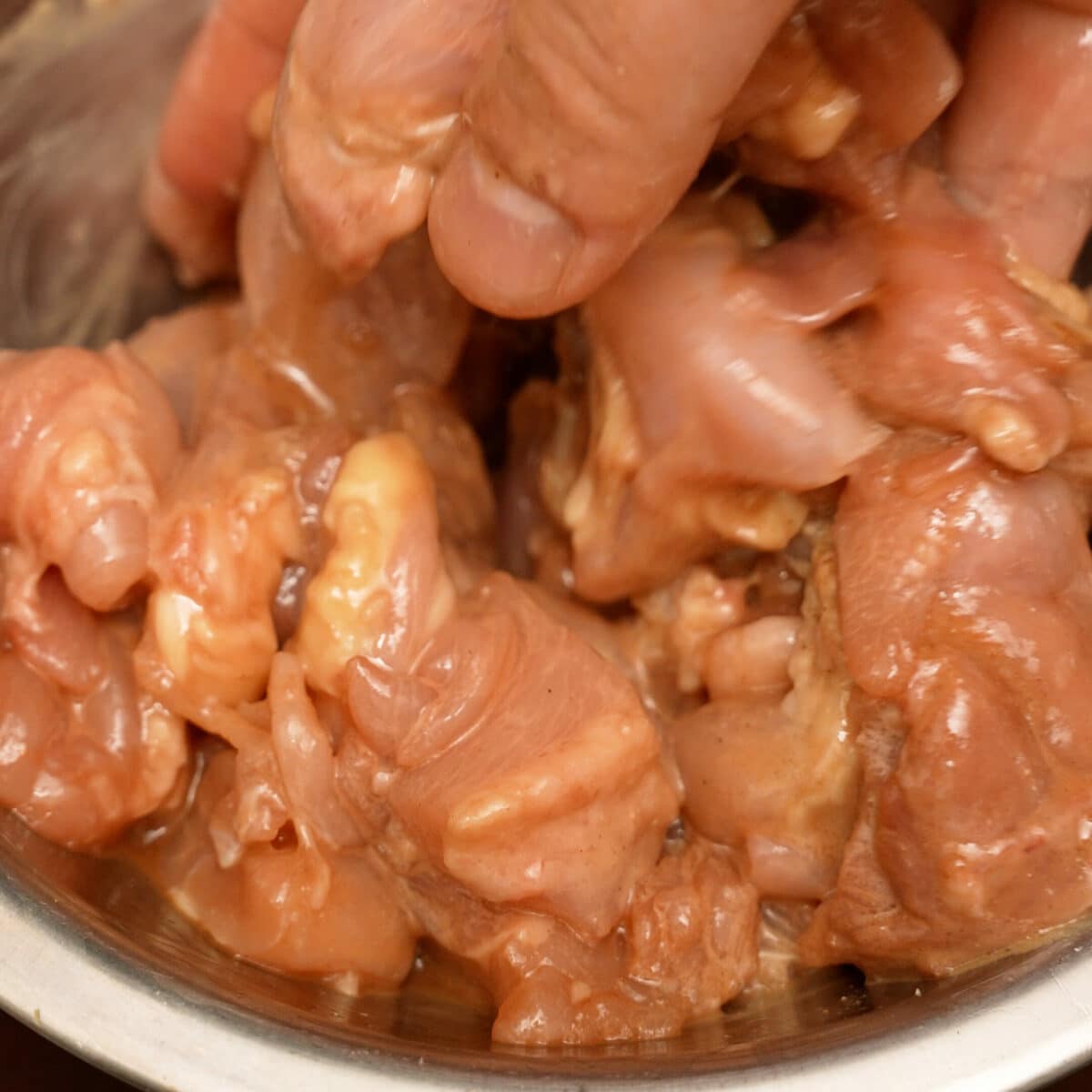 Chicken marinating in a metal bowl.