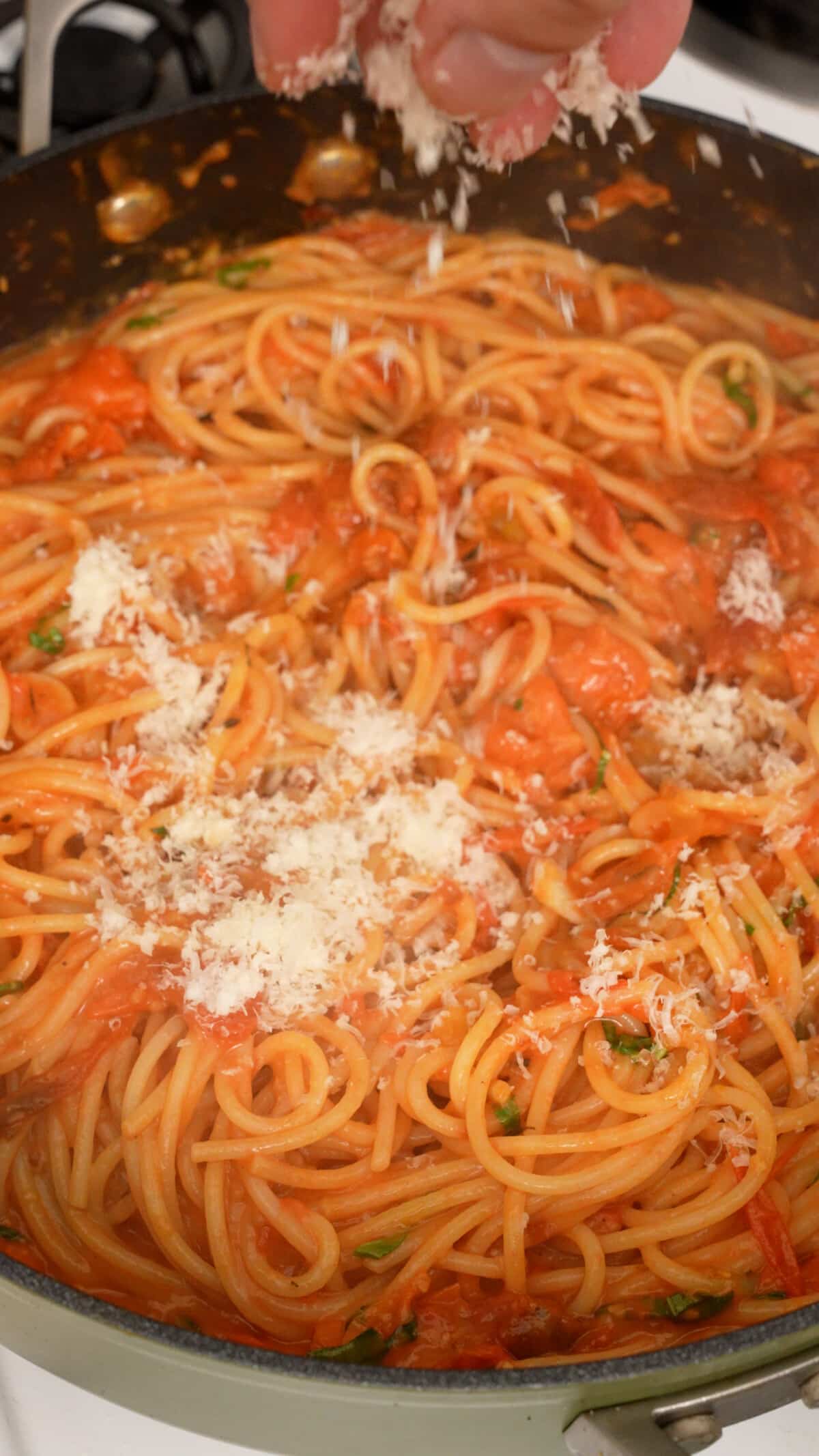 Parmesan cheese being added to the Cherry Tomato Pasta in a pan.