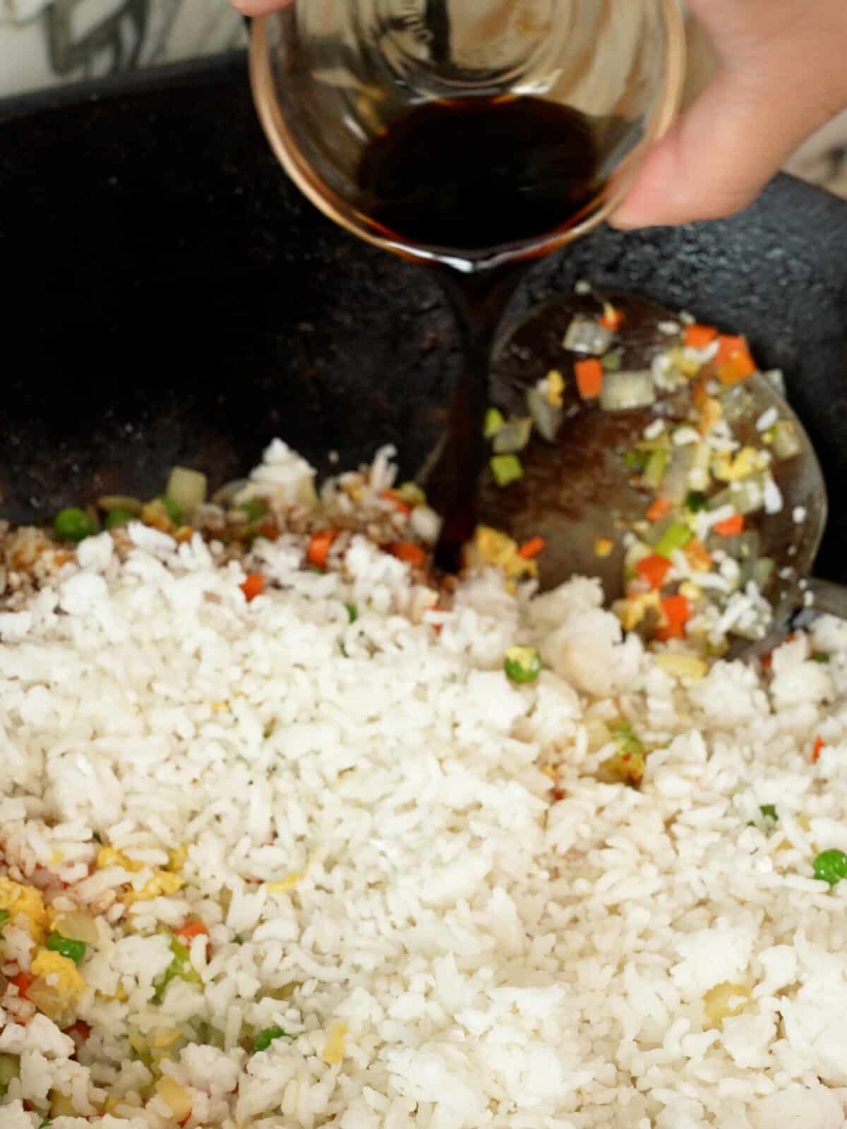 Soy sauce being poured over rice and vegetables in a wok.
