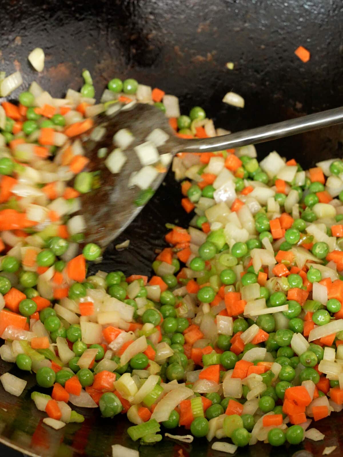 Onions, carrots, peas, and garlic cooking in a wok.