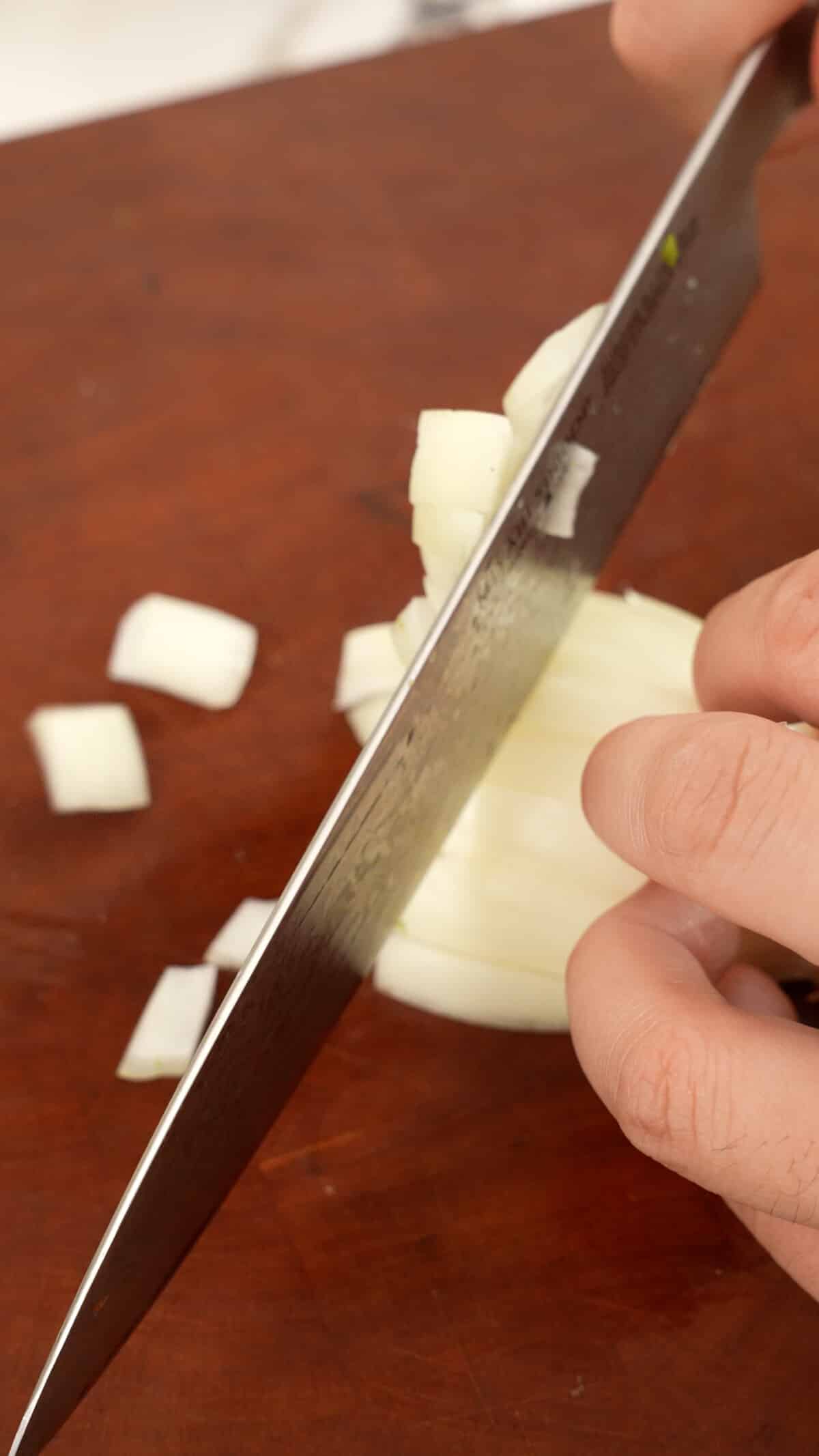 Dicing onions on a cutting board with a knife.