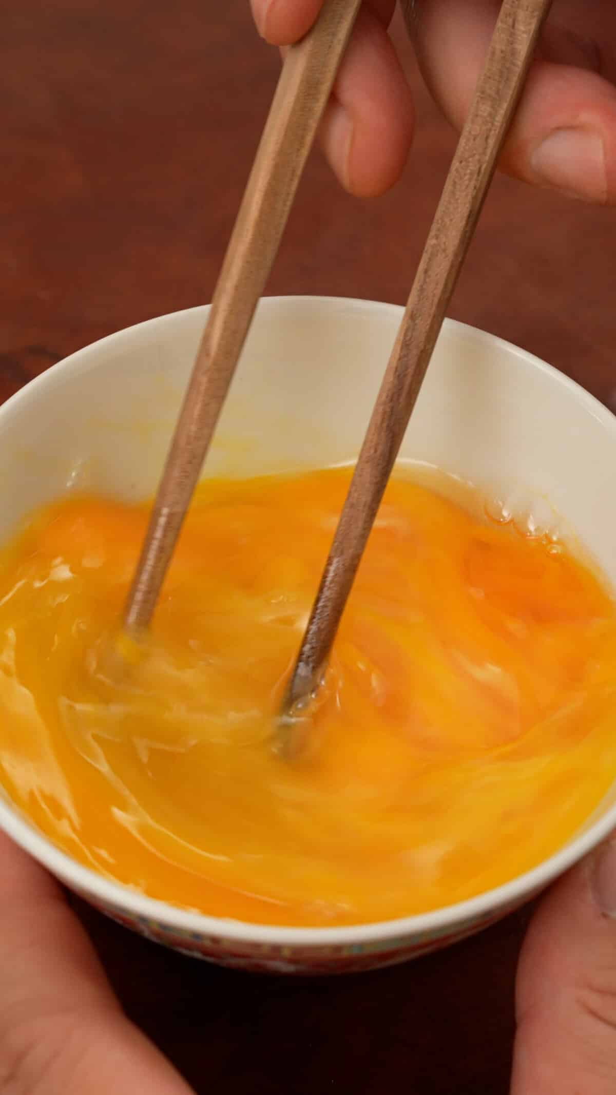 Beating eggs in a bowl with chopsticks.