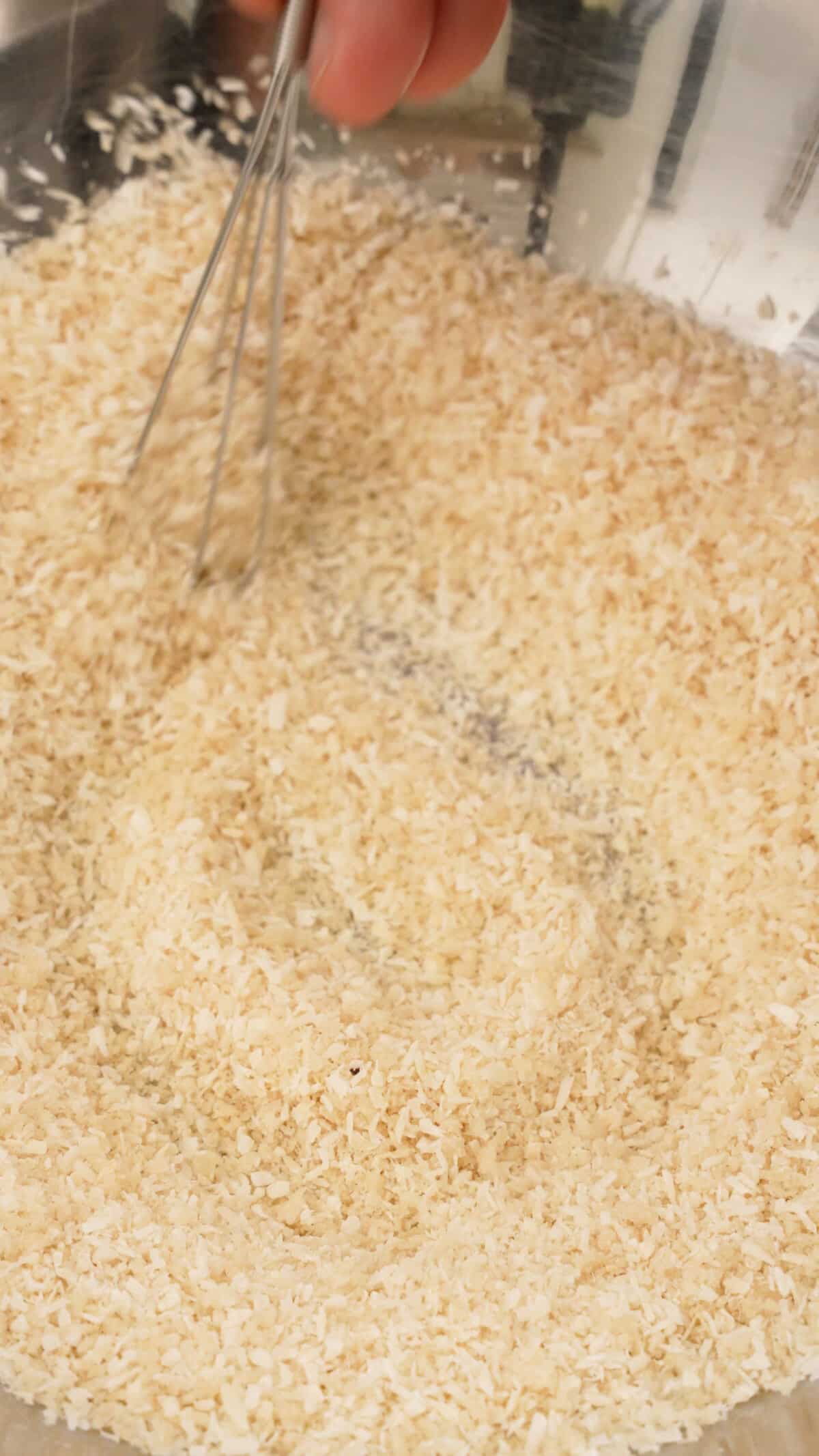 Panko breadcrumbs and coconut flakes being mixed together in a bowl.