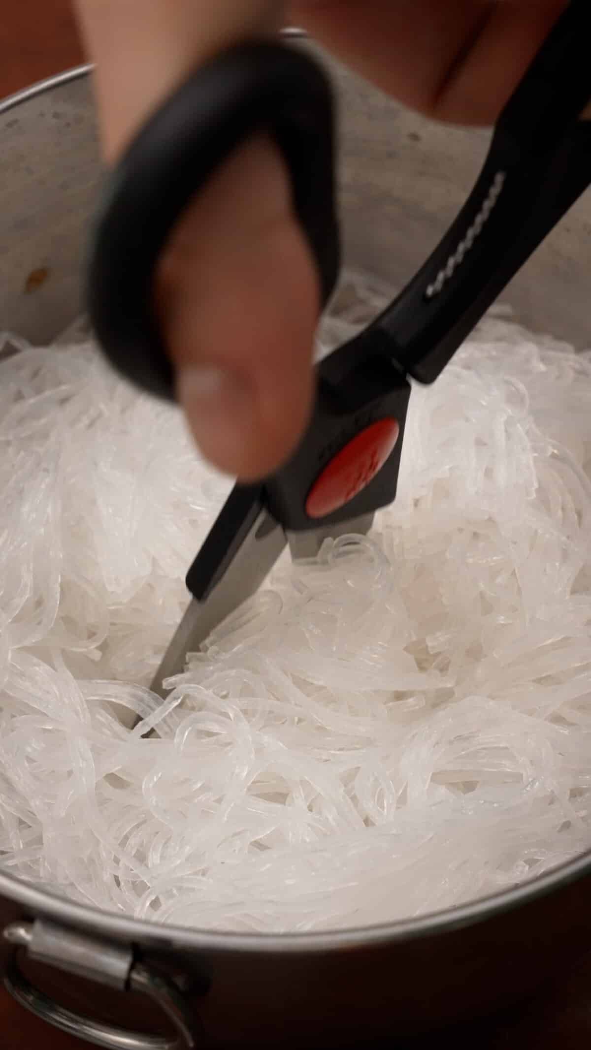 A pair of scissors cutting the rehydrated vermicelli noodles.
