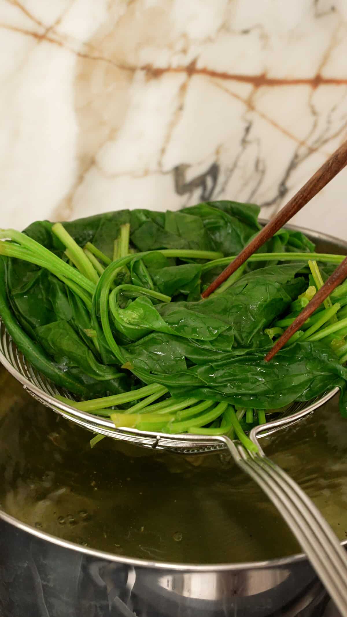 Removing blanched spinach from boiling water with a spider.