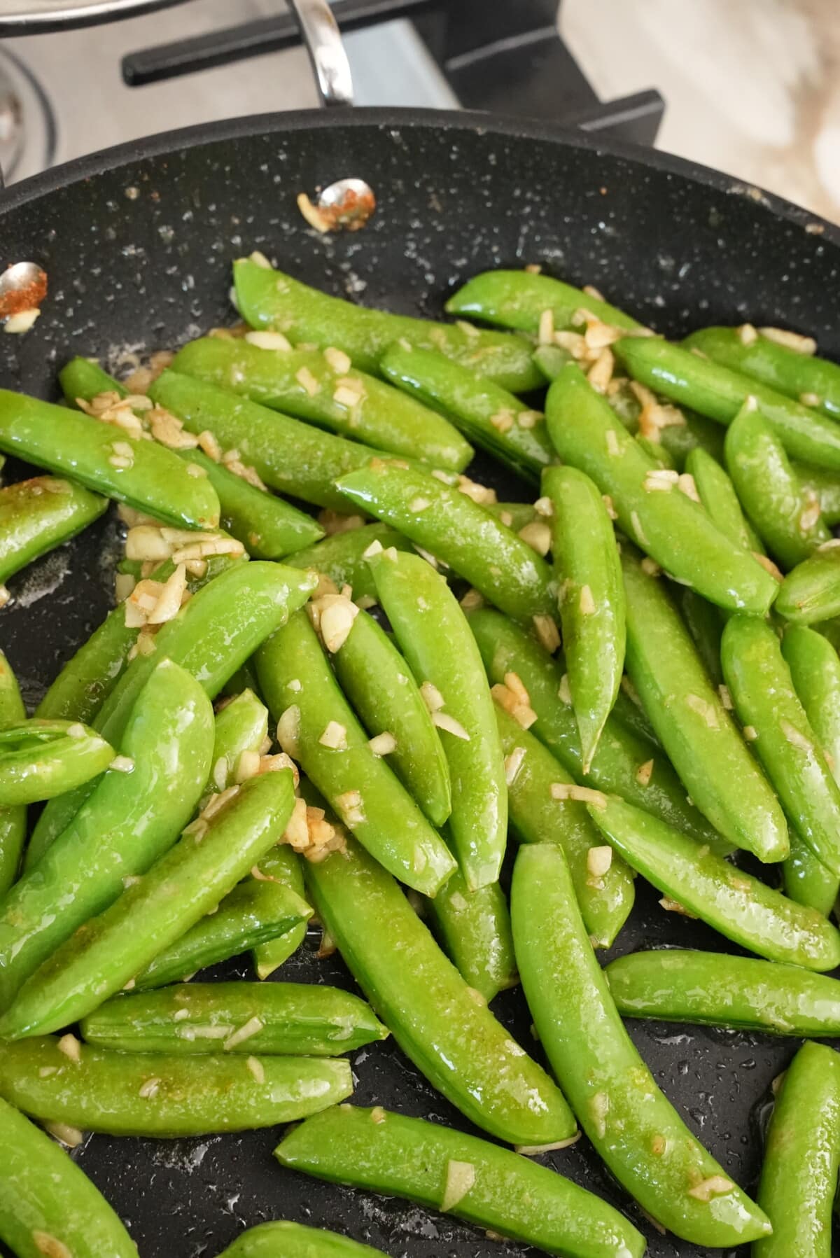 Garlic cooking with snap peas in a pan.
