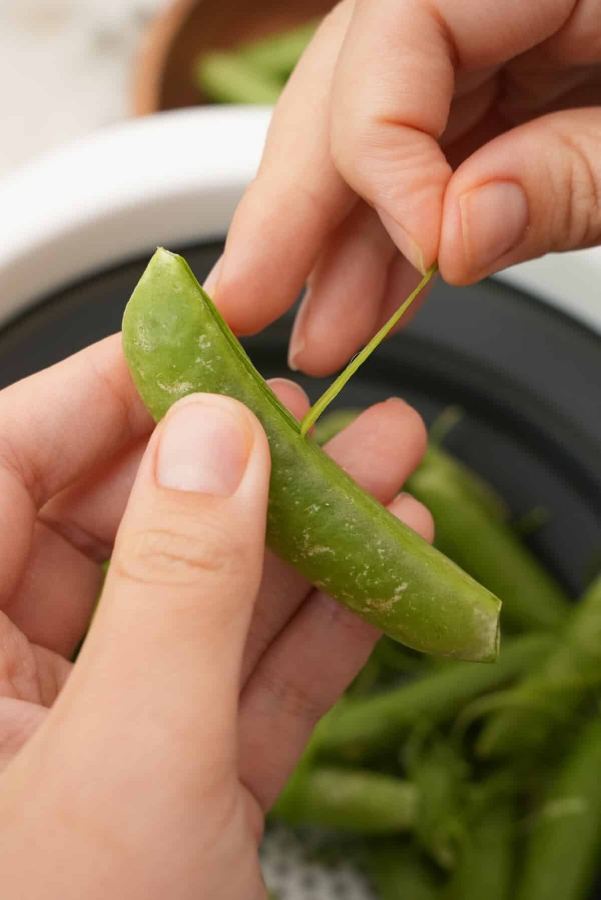 Preparing the snap peas by removing the tough stringy lining.