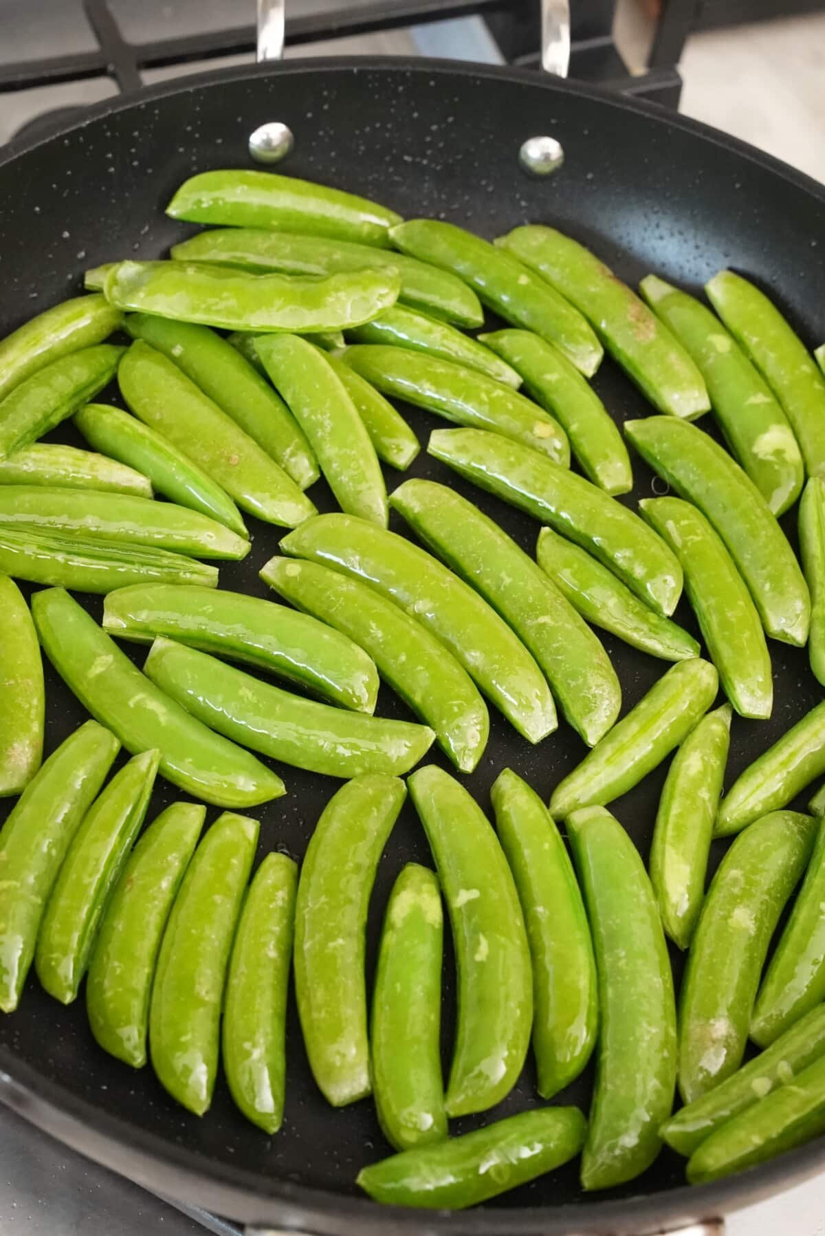 Snap peas sauteing in a pan with oil.