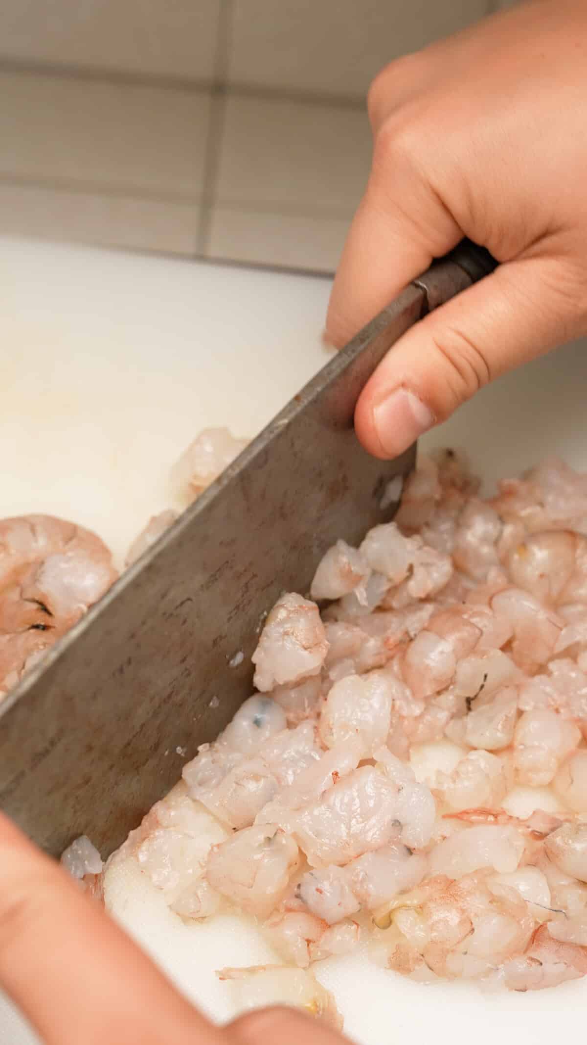 Shrimp on a cutting board being minced by a cleaver.
