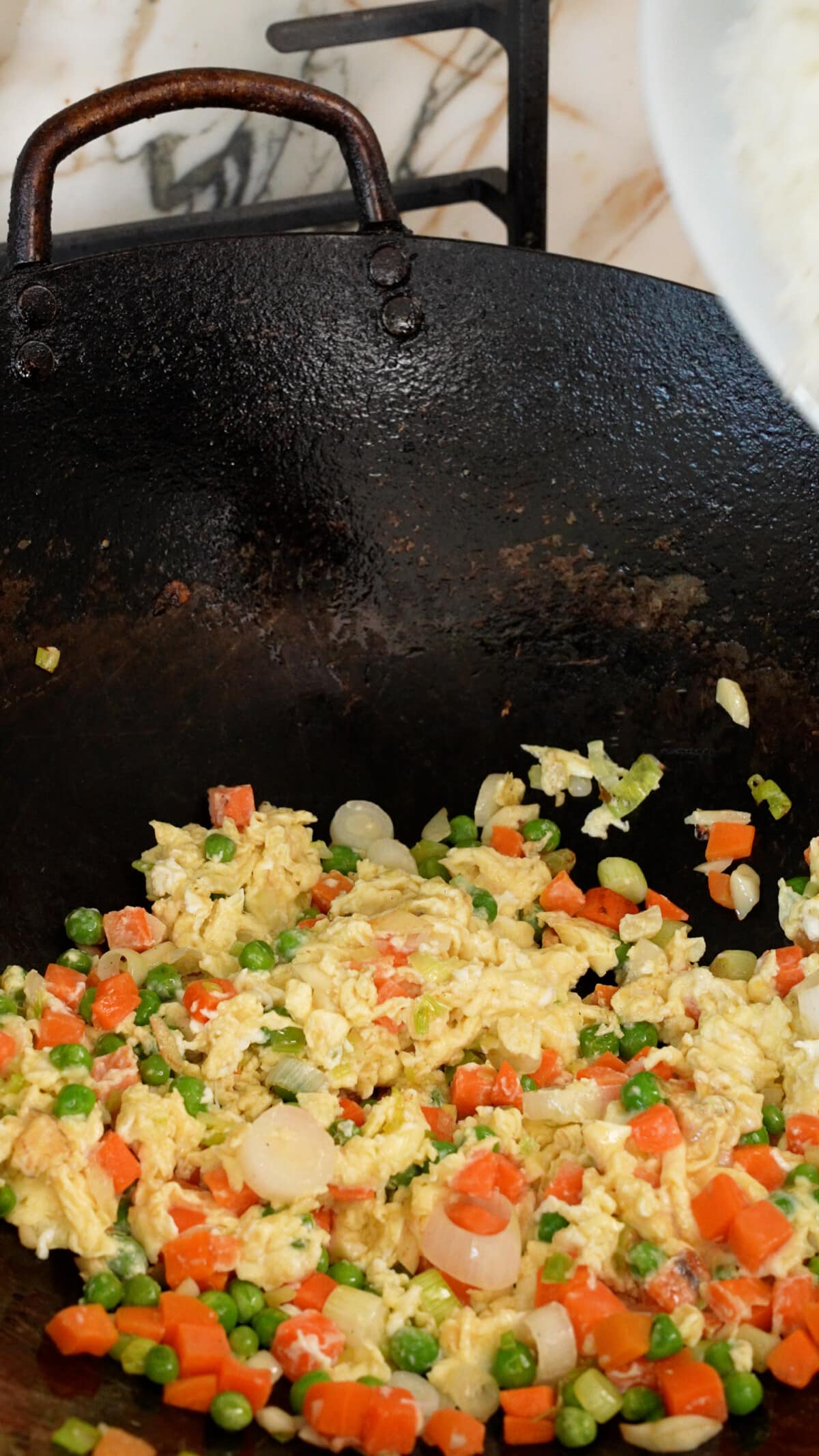 Eggs mixed together with vegetables and aromatics in a wok.