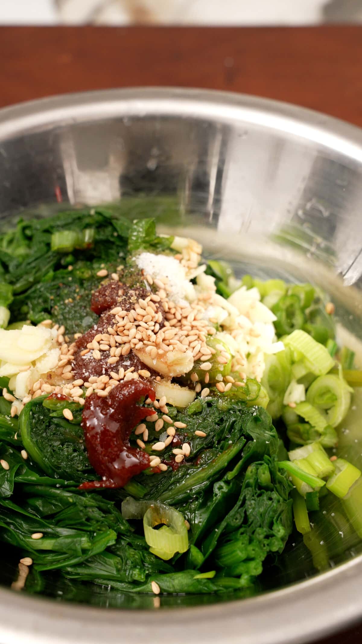 Spinach in a metal bowl marinating to make Spicy Korean spinach side dish.