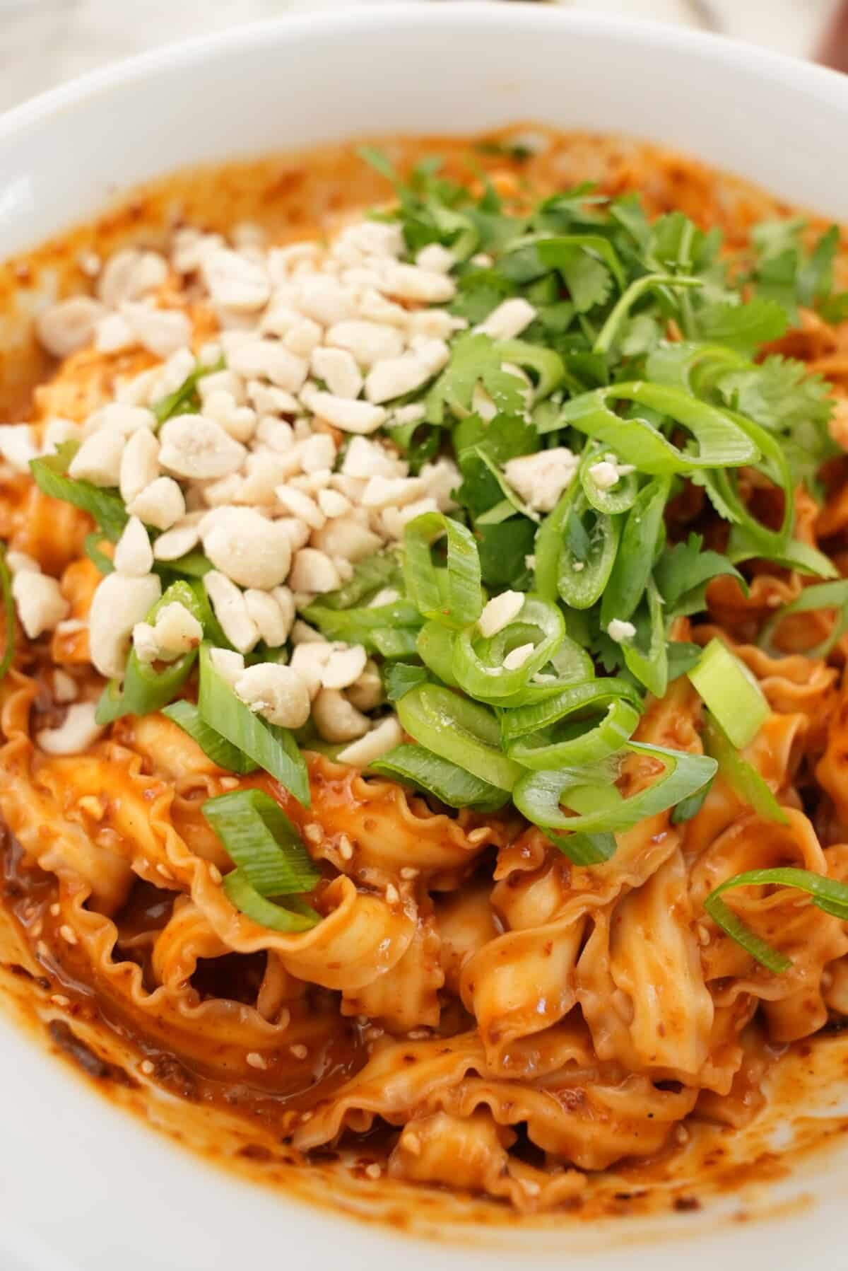 Spicy Peanut Noodles in a bowl topped with peanuts and scallions.