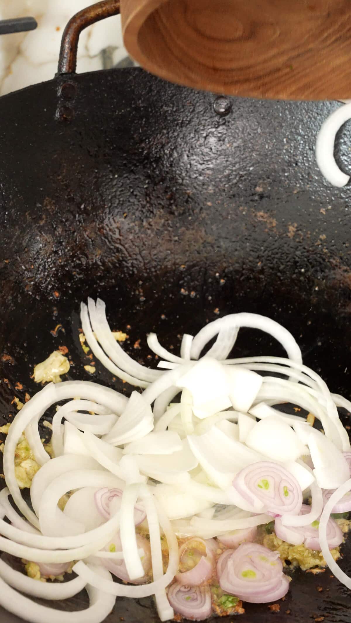 Onions and shallots being added to the wok with thai chili and garlic paste.
