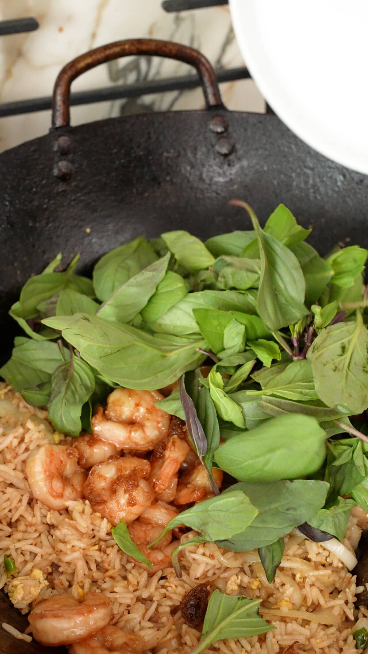 Shrimp and Thai Basil being added to the fried rice in a wok.