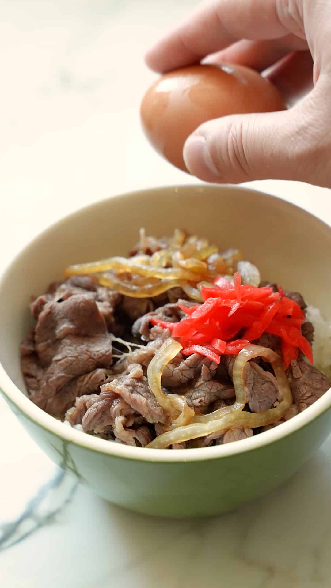 Beef gyudon in a green bowl with onions over rice.