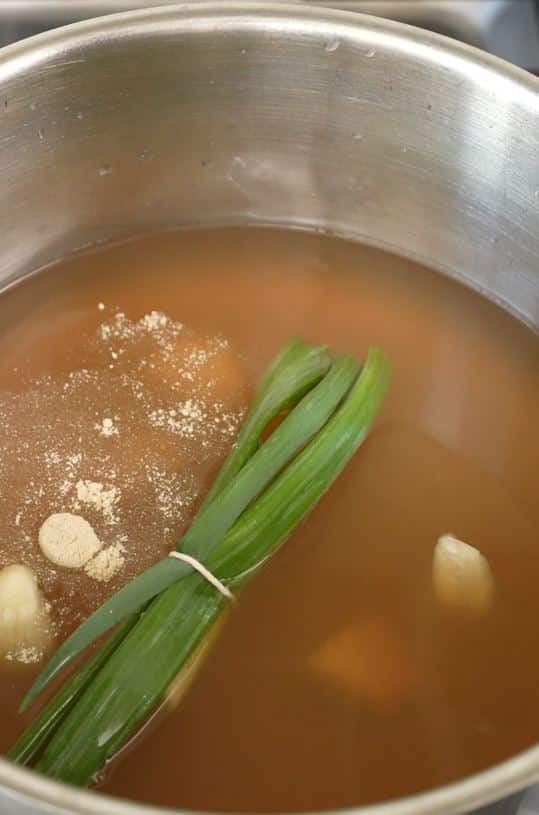 Garlic, ginger, scallions, and white pepper in chicken broth in a pot.