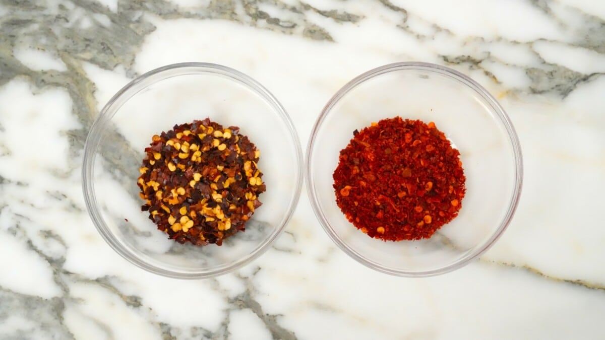 Crushed red pepper flakes and Sichuan chili flakes next to each other in separate glass bowls.