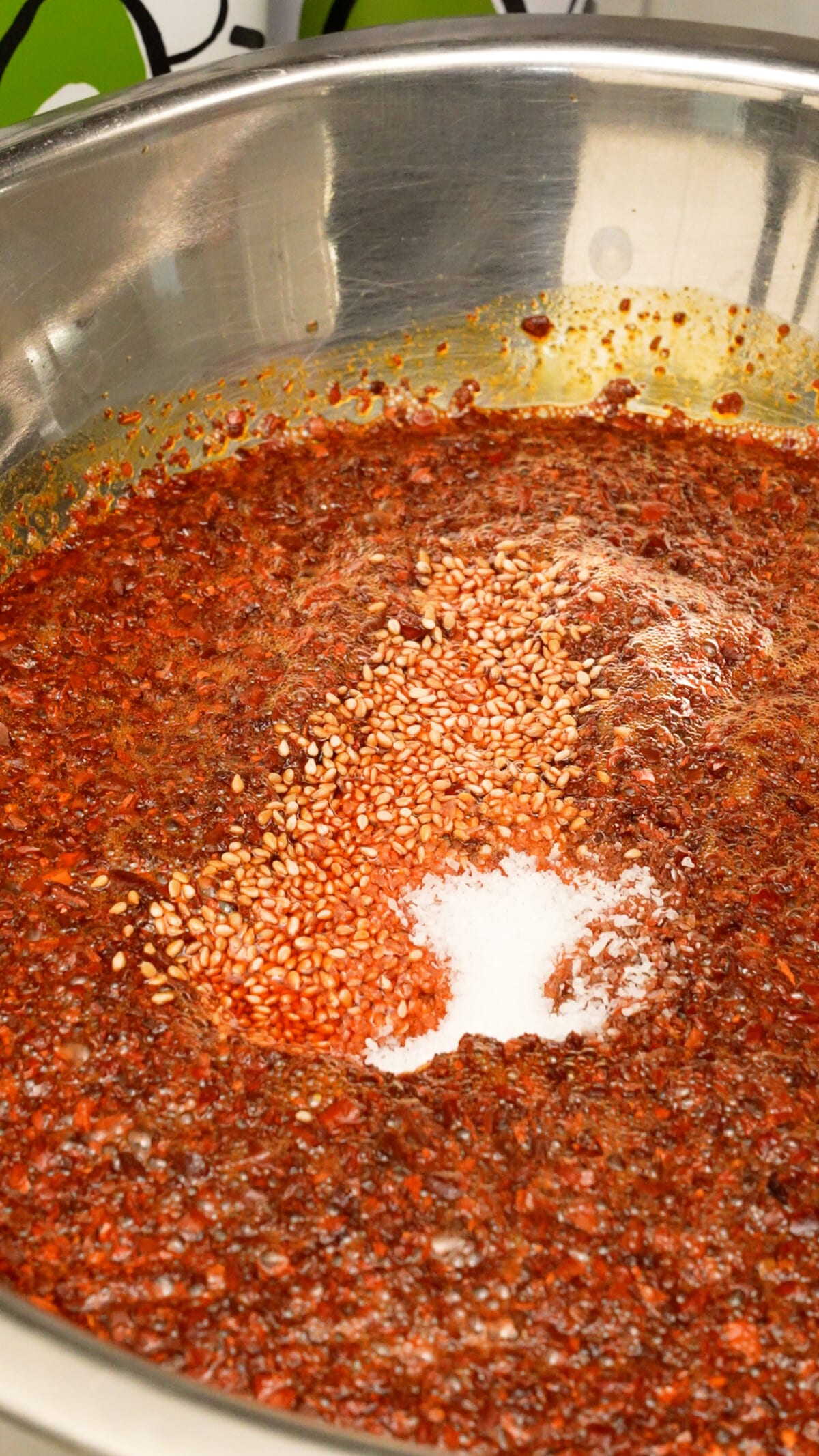 Sesame seeds, salt and sugar being added to chili oil in a metal bowl.