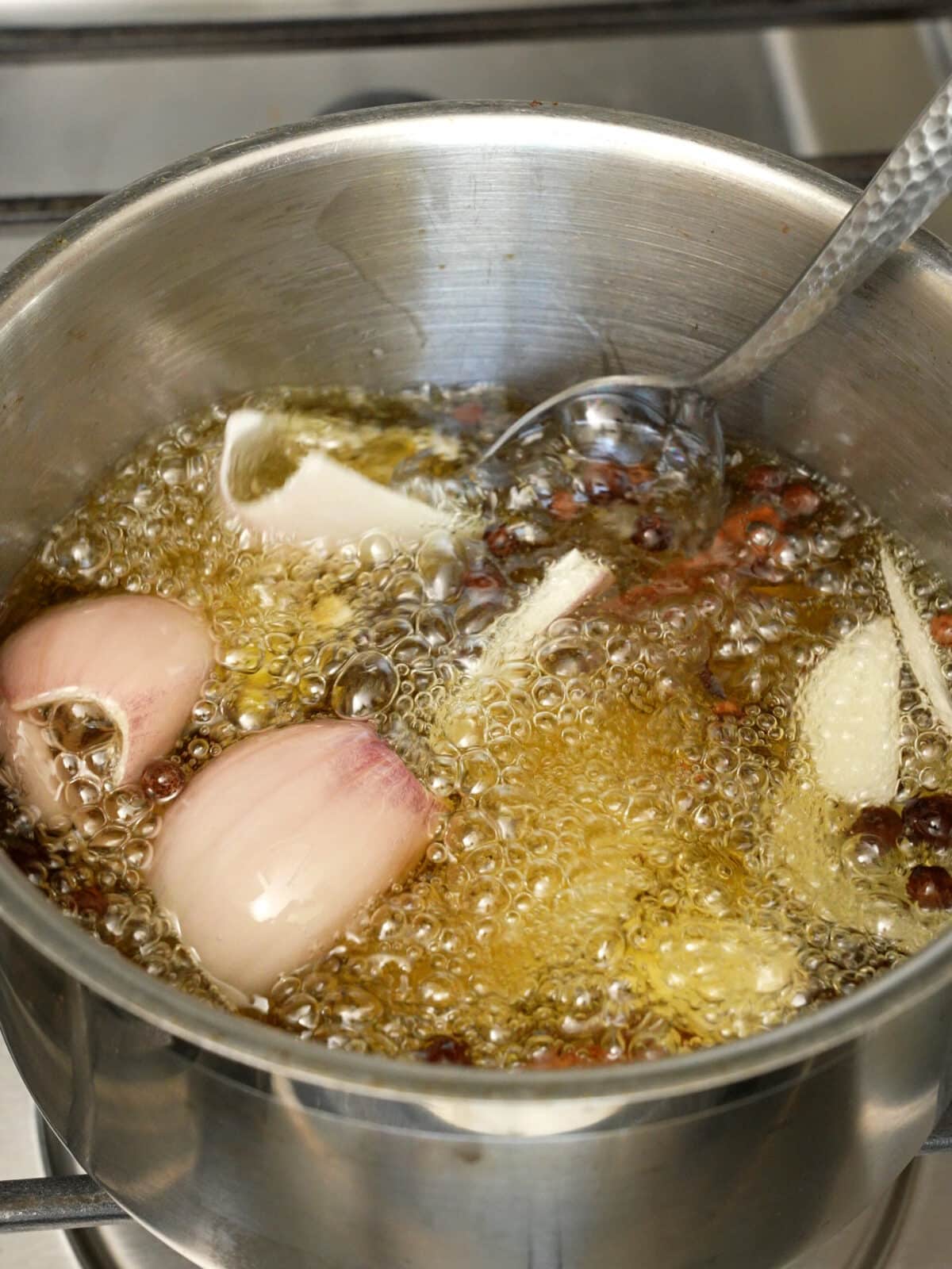 Fresh garlic, ginger, and shallots with dried spices infusing in neutral oil in a small pot.