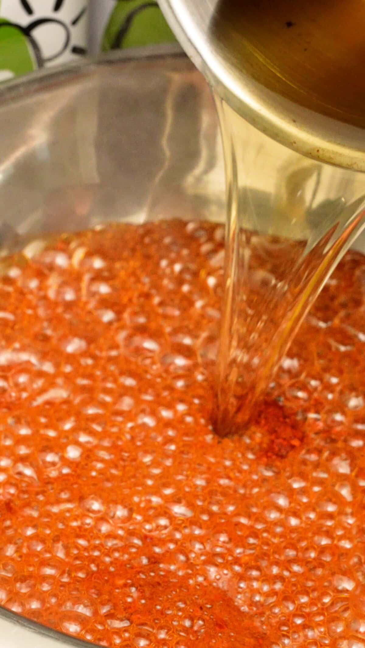Hot oil being poured over Sichuan chili flakes into a metal bowl.