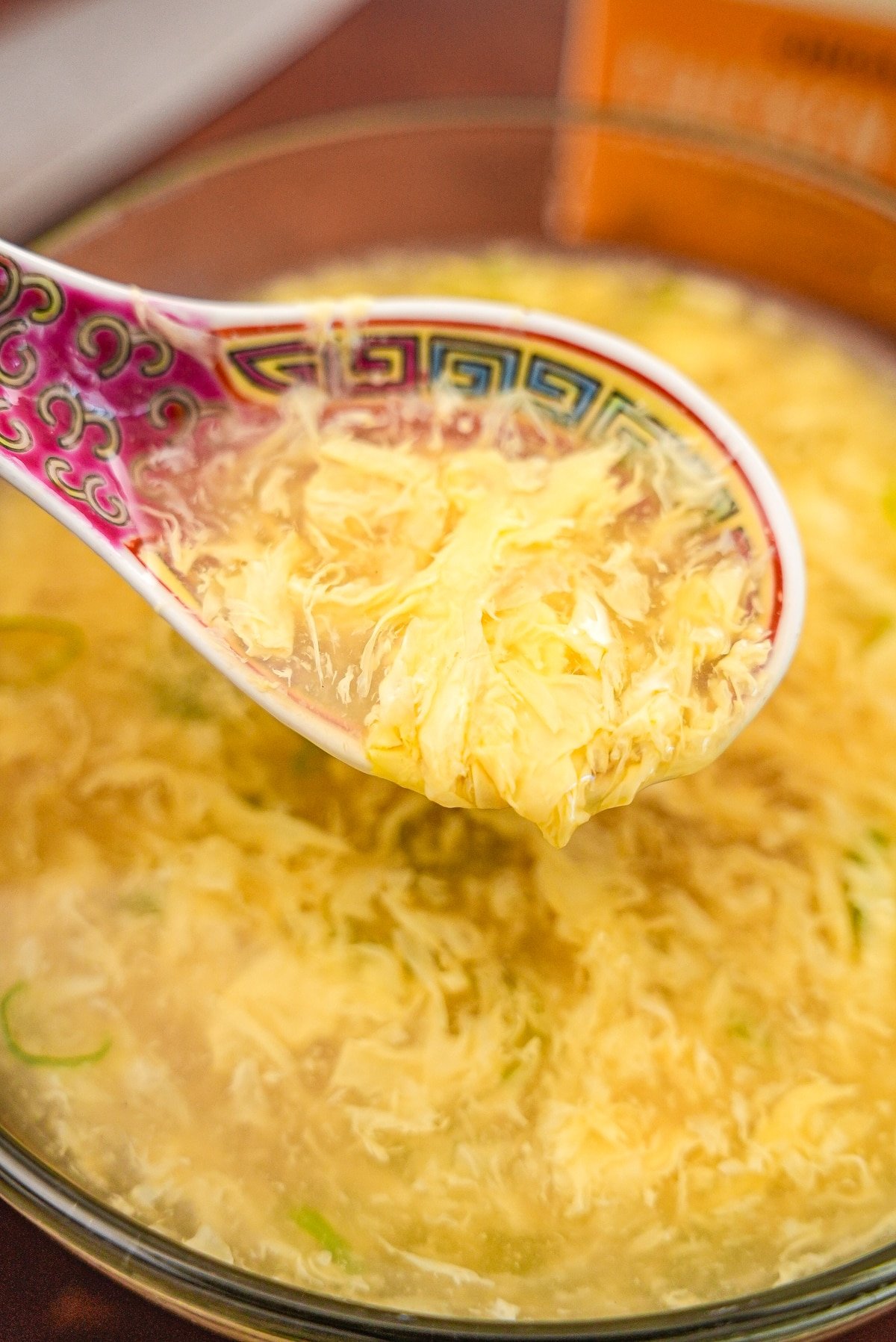 Egg drop soup in a spoon over a glass bowl of soup.